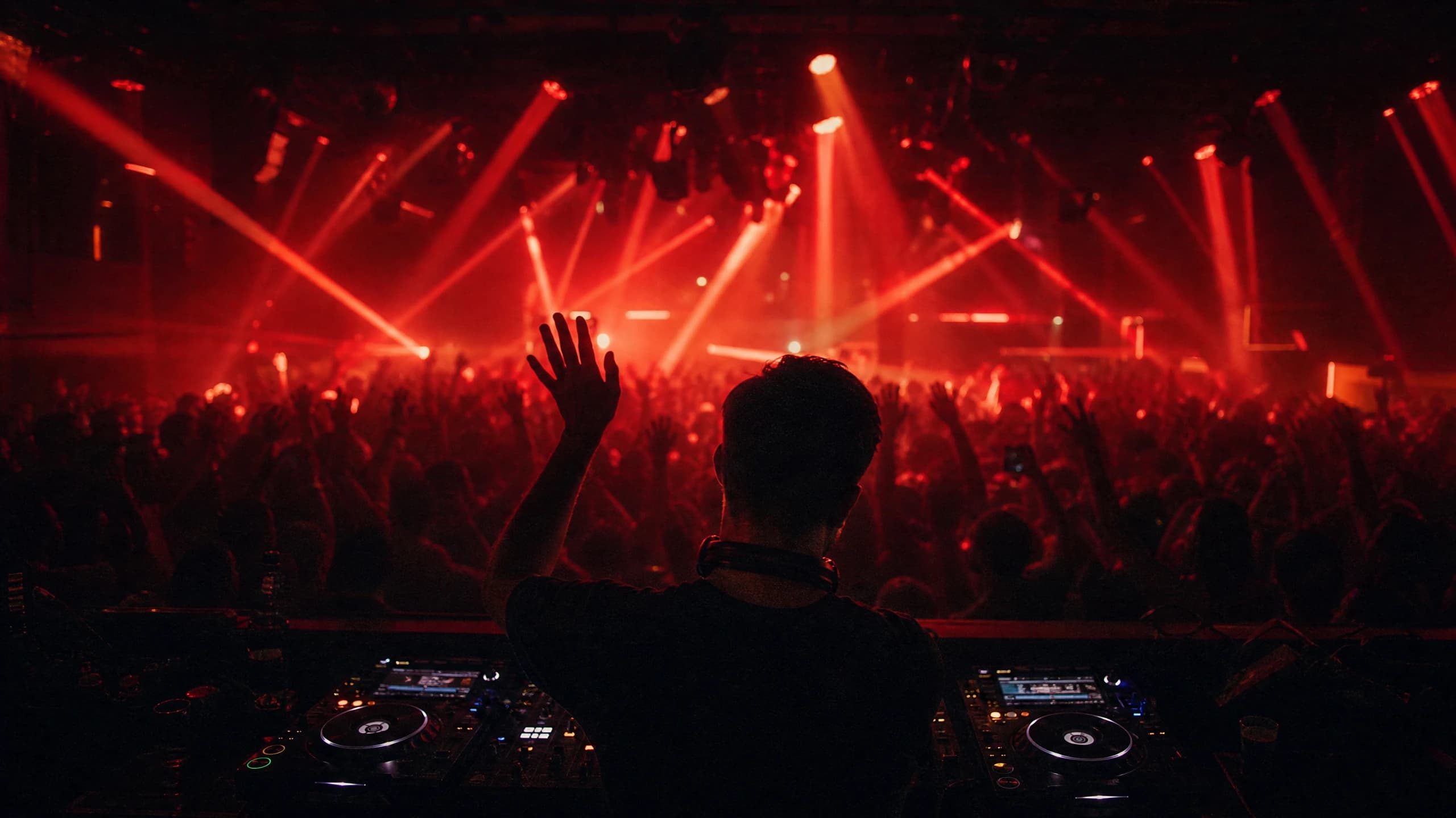 Volle Tanzfläche in einem Club, von hinter dem DJ-Pult fotografiert, mit rotem Licht und Nebel.